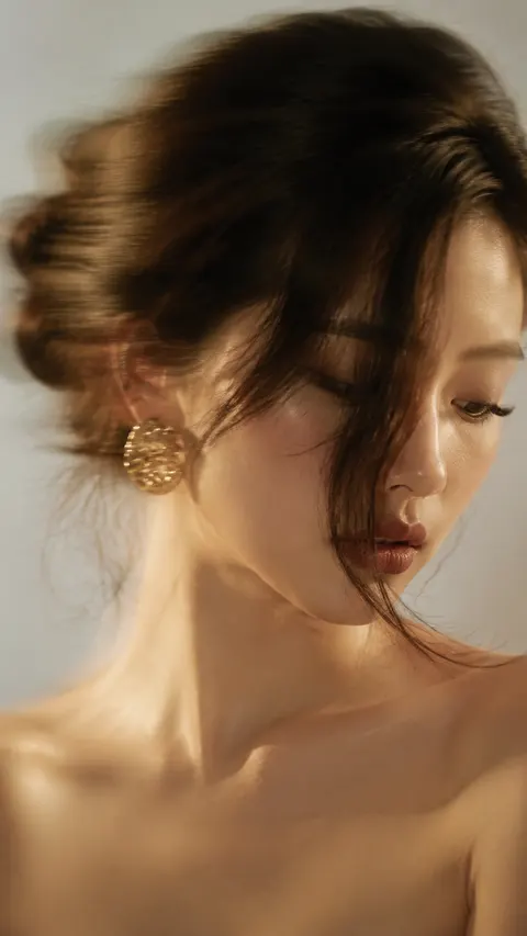 智能手机摄影或长曝光相机拍摄质感，一位中国的年轻女性近距离shotSize: 特写，平视角度构图，subjectPosition: subjectPosition: 脸部略微位于画面中心右侧，垂直 9:16 画幅。她梳着蓬松的编织低发髻，一缕修饰脸型的长发自然垂落并遮住半张脸，低头看向一侧，一只眼睛几乎被发丝遮挡，嘴唇微张，裸露肩膀，atmosphere: 姿态优雅、神秘、富有氛围感。人物妆发细节精致清晰，佩戴醒目的大金耳环，皮肤光滑亮泽，柔和桃色腮红，微妙高光，根根分明的睫毛，productMaterial: 哑光干枯玫瑰色嘴唇搭配深色唇线。color: 背景为中性浅灰色或白色极简空间，无明显道具干扰，柔和自然窗光从侧前方照亮面部，整体呈温暖奶油色金调，柔和对比，暖色调电影级调色。，尤其强化耳环、头发和轮廓边缘的拖影与轻微晃动感，exposureLogic: exposureLogic: 保留时尚编辑大片的电影美学与长曝光质感。画面需高级、干净、极简噪点